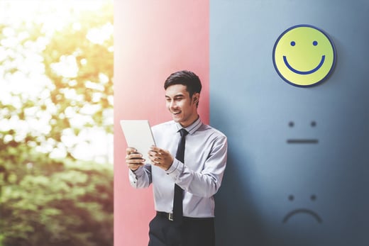 Hombre sonriente con una tablet frente a un mural con varios emojis